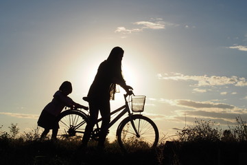 A mother and her daughter walk along a country road with a bicycle to back their home in the evening of winter: silhouette photo
