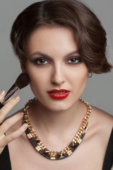 Beautiful woman with evening make up surrounded by the different brushes for make up