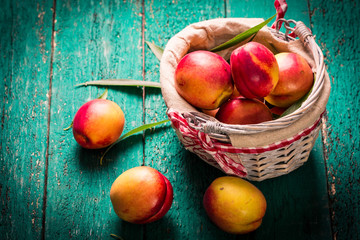 Fresh peaches in a basket on rustic wooden table.