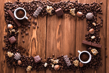 Roasted coffee beans, chocolate, candy, nuts, cup and the frame for inscriptions on wooden background