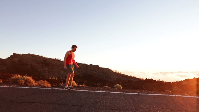 Runner - athlete man running training outdoors exercising on mountain road at sunset in amazing landscape nature. Fit handsome athletic male working out for marathon run outside in summer.