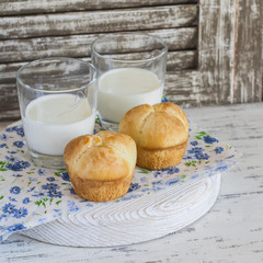 Buns and glasses of milk on a light rustic wood background.