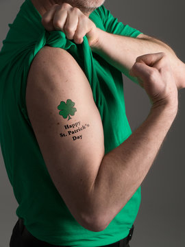 Photograph Of A Man In A Green T Shirt Pulling Back His Shirt Sleeve To Reveal A Shamrock Tattoo With A 