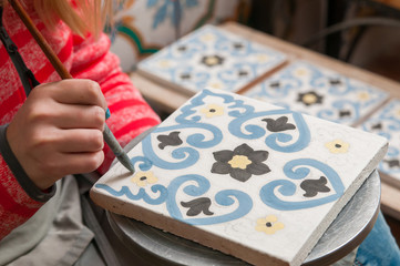 A pottery decorator painting a ceramic tile with floral motifs in his work table in Caltagirone,...
