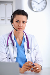 Doctor wearing headset sitting behind a desk with laptop over grey background