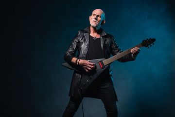 Fototapeta premium Bald heavy metal senior man with electric guitar in front of dar