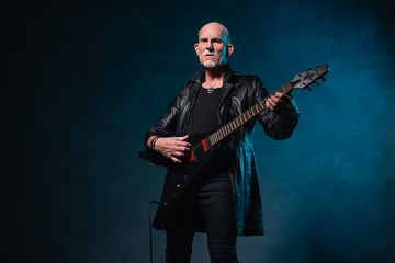 Bald heavy metal senior man with electric guitar in front of dar