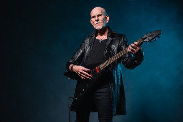 Bald heavy metal senior man with electric guitar in front of dar