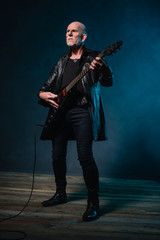 Fototapeta premium Bald heavy metal senior man with electric guitar in front of dar