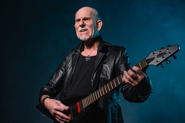 Bald heavy metal senior man with electric guitar in front of dar