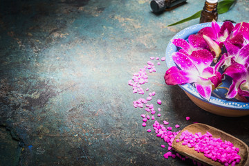 Bowl with water and purple orchid flowers on dark background with shovel of sea salt. Spa, wellness or body care concept.