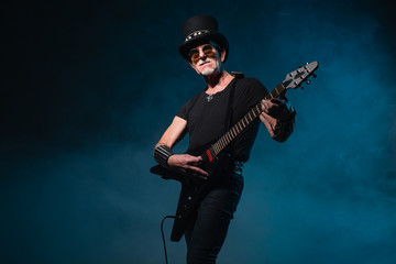 Fototapeta na wymiar Heavy metal senior man with electric guitar in front of dark blu