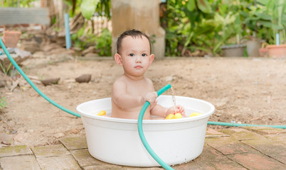 Asian baby boy outdoor bathing in the white bathtub . He is smiling and playing yellow duck full of happiness, Country side culture of Thailand