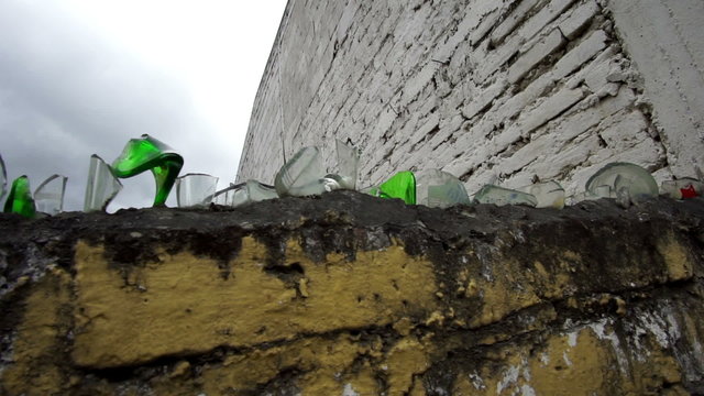Handheld close up shot of a brick wall in a Latin American country topped with pieces of sharp and pointy broken bottle glass reused for deterrence and security measures.