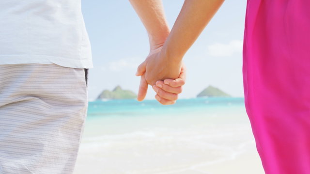Beach couple in love holding hands on honeymoon. Pink dress, casual beachwear romantic newlyweds people standing on travel summer vacations on Lanikai beach, Oahu, Hawaii, USA with Na Mokulua Islands.