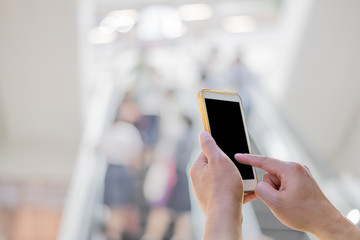 Man using touch screen mobile phone with Blurry Escalator in a m