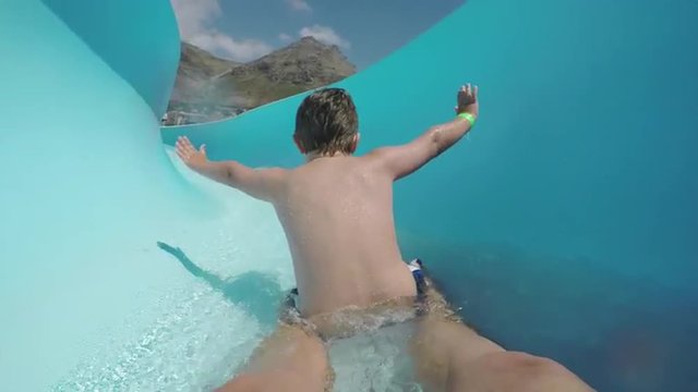 Happy young boy going down curved waterslide in slow motion Cape Town
