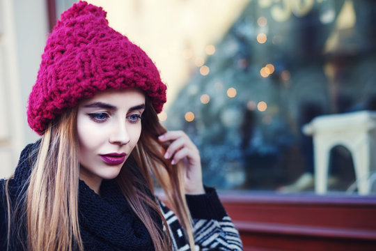 Street portrait of young beautiful woman with long blond hair wearing stylish winter hat. Model looking down. Female fashion concept. Close up. Toned