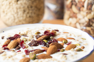 A bowl of yoghurt and breakfast cereal with bottles of cereal, nuts and raisins in the background