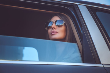 A woman in sunglasses looking through car's window. - obrazy, fototapety, plakaty