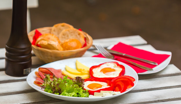 Two fried eggs with ham, vegetables and cheese served on a white plate, ready for consumption