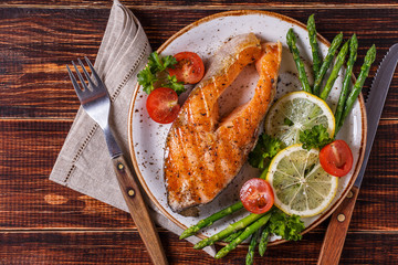 Grilled salmon steak served with asparagus, tomato and lemon.