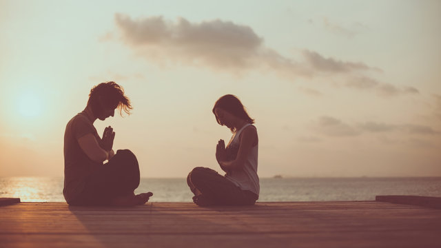 Young couple is doing yoga on the sunrise background.