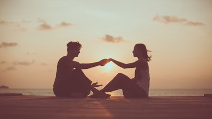 Young couple is doing yoga on the sunrise background.