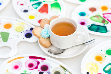 cup with tea and cookie surrounded watercolor palette