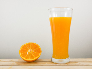 The glass of tasty pure orange juice and fresh orange half on wooden tray for a good healthy.