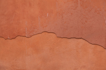 Old terracotta painted stucco wall with cracked plaster. Backgro