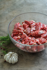 Chunks of raw lamb meat with spices in glass plate over old wood