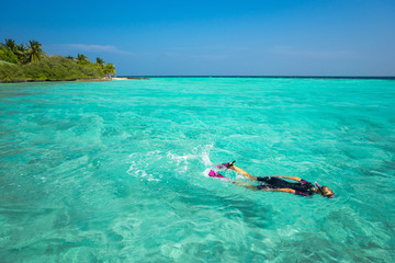 Woman snorkeling in clear tropical waters in front of exotic isl