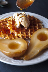 Waffles, pears cooked in sugar syrap and ice cream on white plate