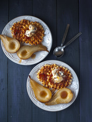 Waffles, pears cooked in sugar syrap and ice cream on white plate, spoons on blue wooden table