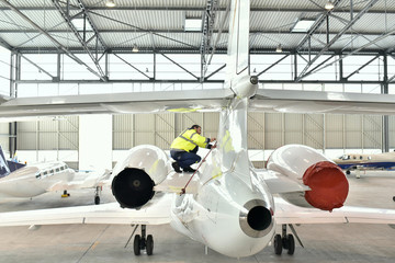 Mechaniker kontrolliert Aussenhülle am Triebwerk eines Flugzeugs im Hangar - professionelle Flugzeugreparatur // Mechanics controlled aircraft in the hangar - professional aircraft repair - obrazy, fototapety, plakaty