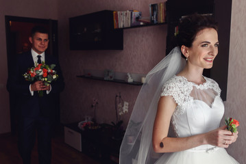 Handsome groom and beautiful bride posing with flowers in hotel