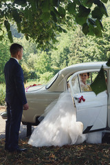 Beautiful brunette bride in retro white car looking at handsome