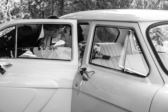 Beautiful brunette bride in retro white car kissing handsome gro