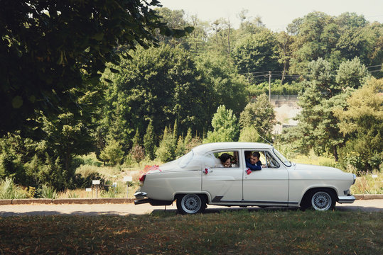 Bride & groom in beautiful retro white wedding car in green park