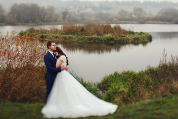 Happy beautiful couple of newlyweds hugging near romantic lake c