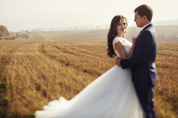 Romantic fairytale newlywed couple hug & smile in field at sunse
