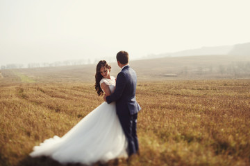 Romantic fairytale newlywed couple hug & smile in field at sunse