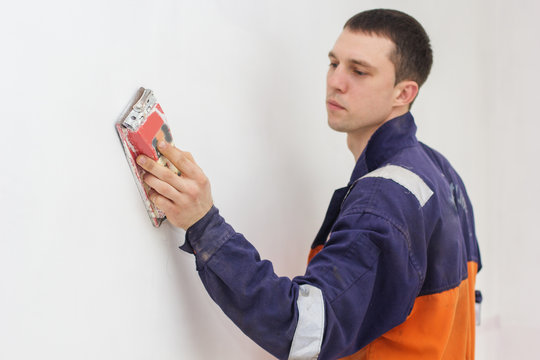 Handyman Grinding With Sandpaper On A White Wall