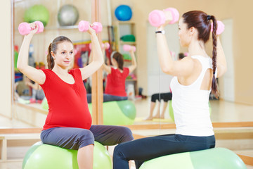 pregnant woman with instructor doing fitness ball exercise