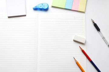 Blank notebook with pencil, red pencil, pen, tag papers, notepad, correction tape, and eraser on white background.