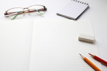 Naklejka premium Blank notebook with pencil, red pencil, glasses, notepad, and eraser on white background. 