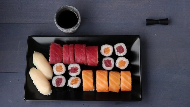 Sushi set nigiri and rolls on black plate served with chopsticks, soy sauce, wasabi and ginger. Flat lay