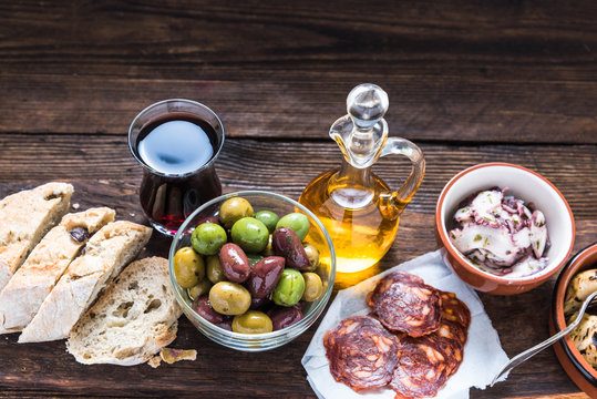 Wooden board with tapas, olives and salami and olive oil
