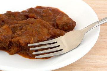 Braised beef on a plate with fork atop wood table